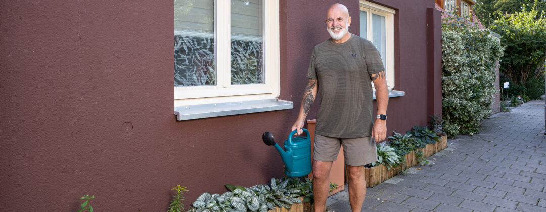 Man met gieter bij geveltuin blij met tuin en Tegelservice Amsterdam Weerproof