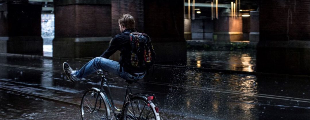 Fietser houdt benen omhoog en rijdt door plas Amsterdam Weerproof