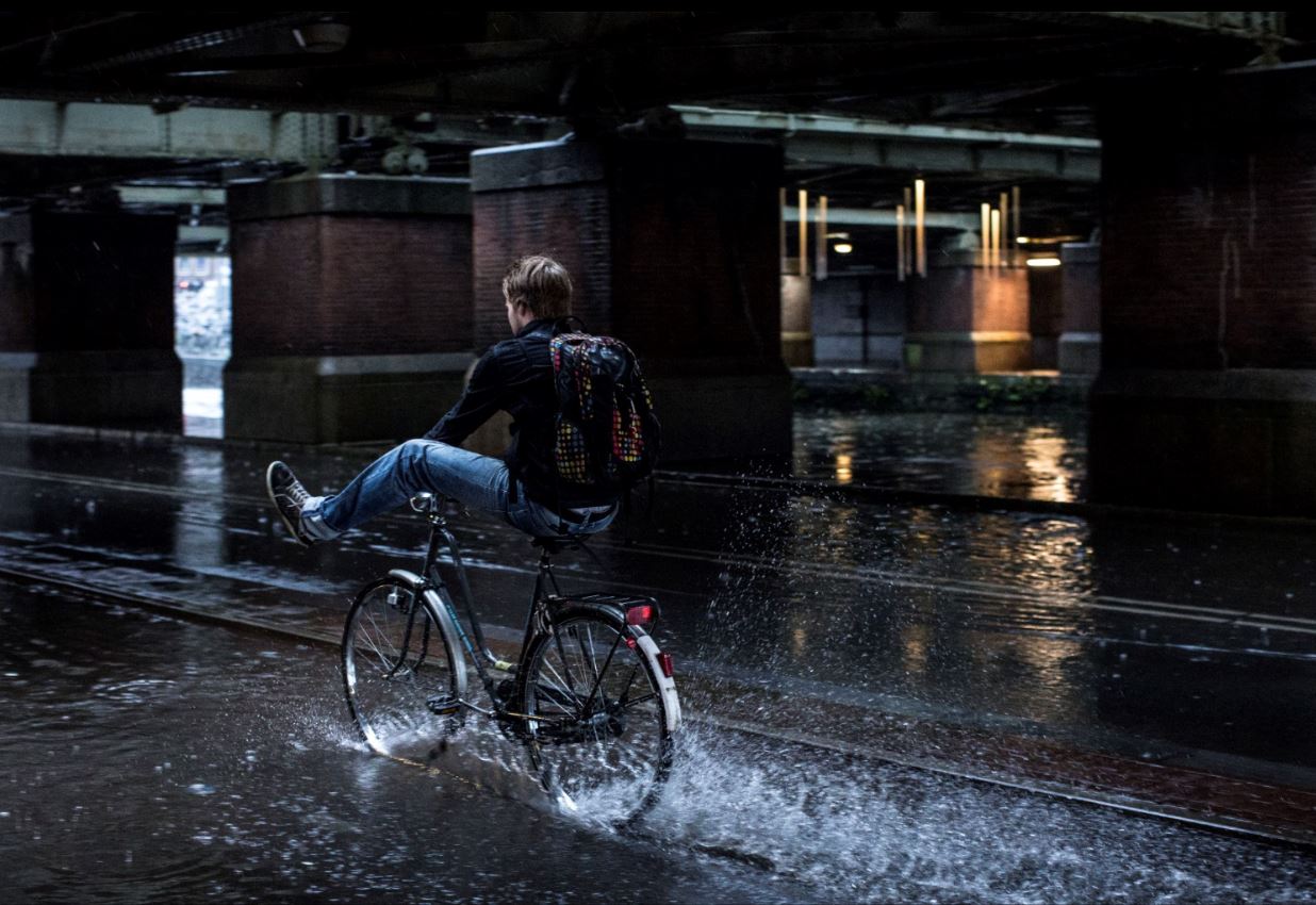 Fietser houdt benen omhoog en rijdt door plas Amsterdam Weerproof