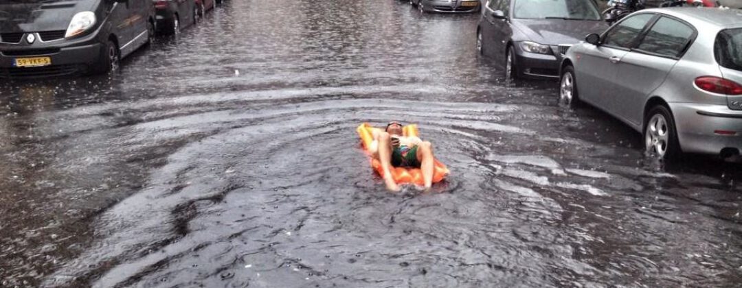 Man ligt op luchtbed in regenplas in extreme neerslag Amsterdam Weerproof