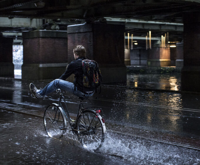 fietser houdt benen omhoog door water op fietspad Amsterdam Weerproof