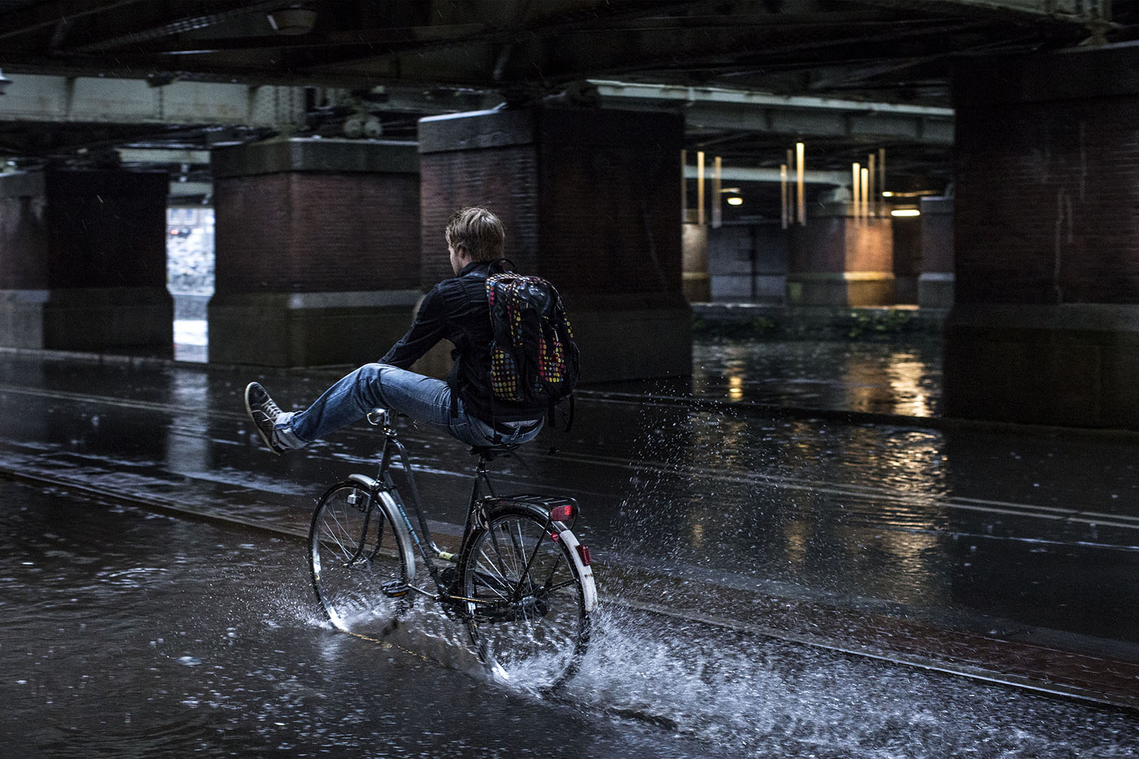 fietser houdt benen omhoog door water op fietspad Amsterdam Weerproof