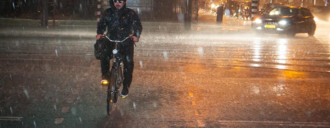 Fietser en auto rijden door extreme neerslag in Amsterdam Weerproof