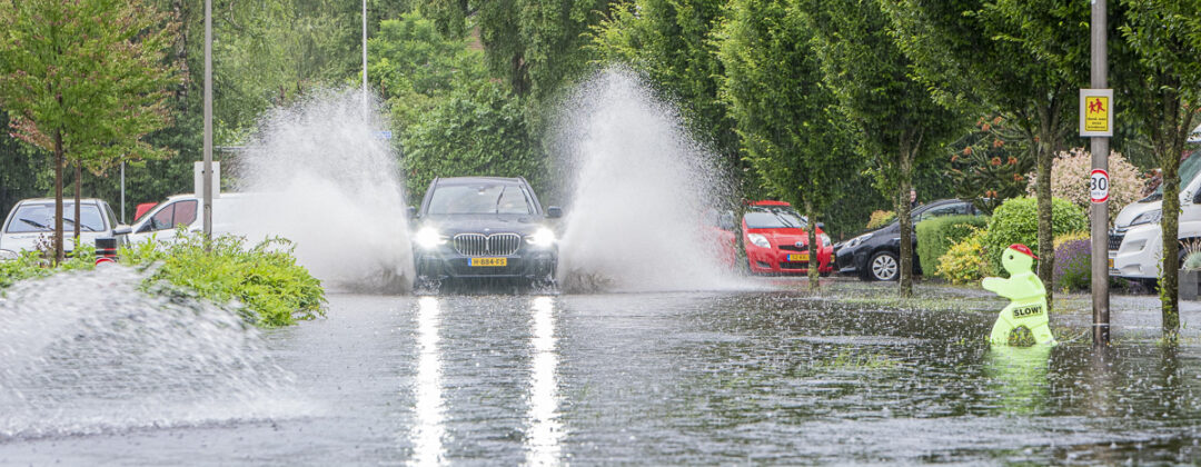 Auto rijdt door grote plassen op parkeerplaats tijdens extreme neerslag Amsterdam Weerproof