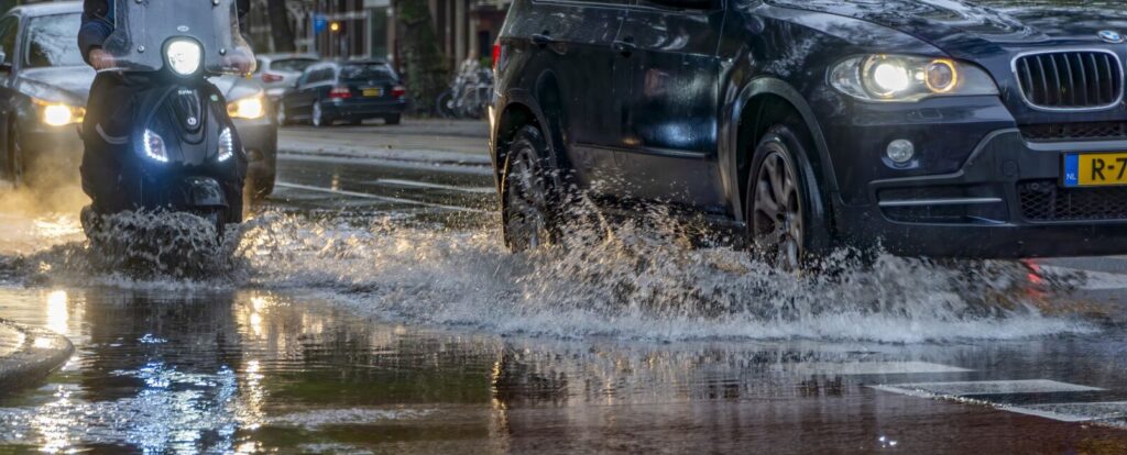 Auto en scooter rijden door grote regenplas Amsterdam Weerproof