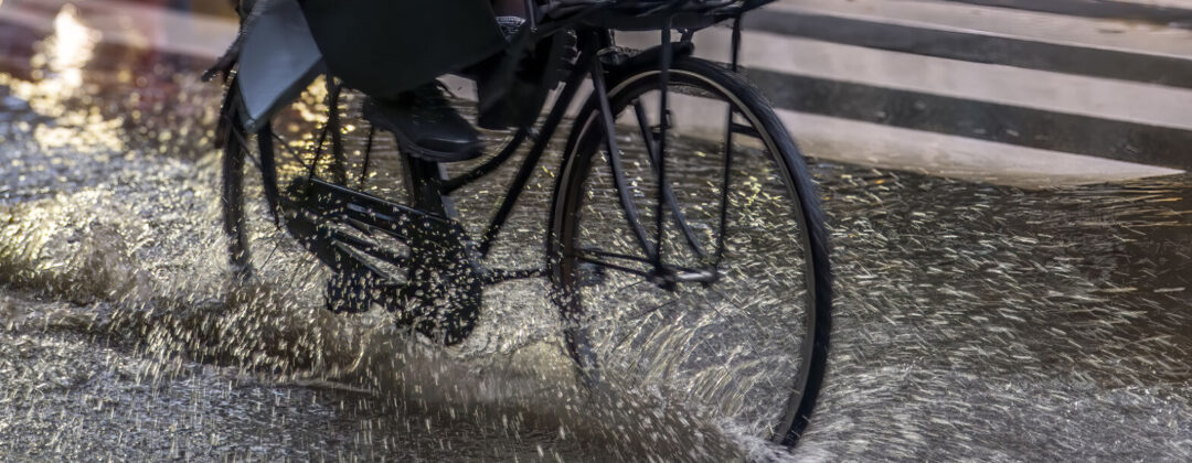 Fietser rijdt door regenplas met voeten omhoog Amsterdam Weerproof