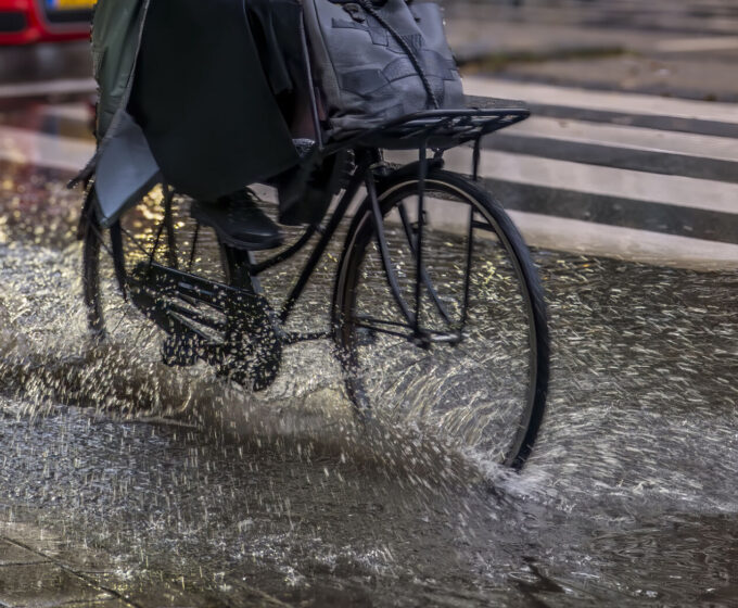 Fietser rijdt door regenplas met voeten omhoog Amsterdam Weerproof