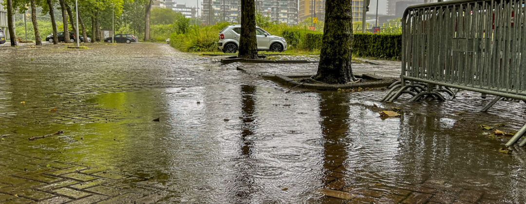 Grote plas met regendruppels op parkeerplaats Amsterdam Weerproof